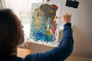 Odaklanmış erkek sanatçı palet bıçağıyla tuvale boya sürüyor.