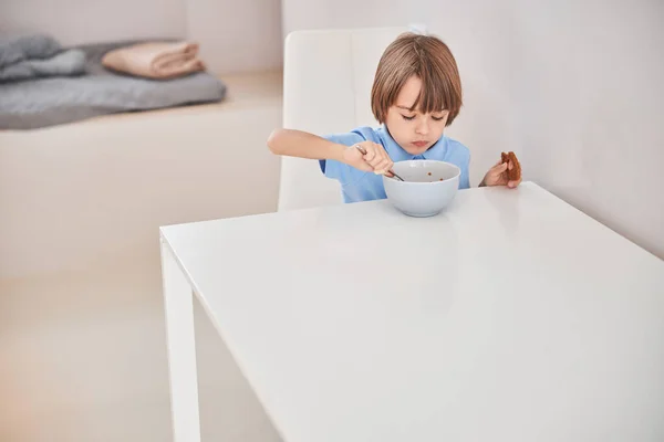 テーブルに座っている間に朝食を取っている小さな子供 — ストック写真