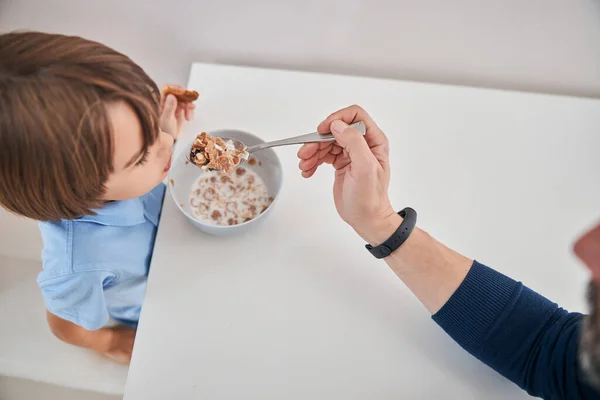 かわいい子供が台所のテーブルに座って餌を与えられて — ストック写真