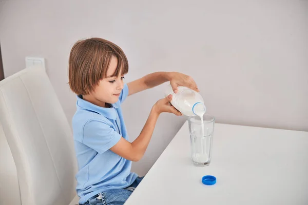 Carino ragazzo versando il latte in un bicchiere alto — Foto Stock