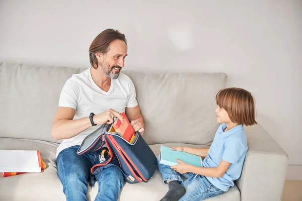 Papá útil y lindo niño sacando libros de la mochila — Foto de Stock