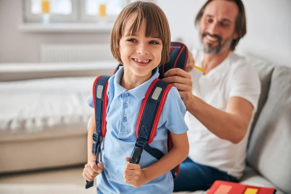 Szczęśliwy dzieciak z plecakiem stojący obok radosnego ojca — Zdjęcie stockowe