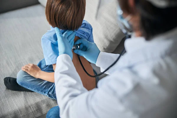 Pediatra cualificado con un estetoscopio que trata a un niño — Foto de Stock