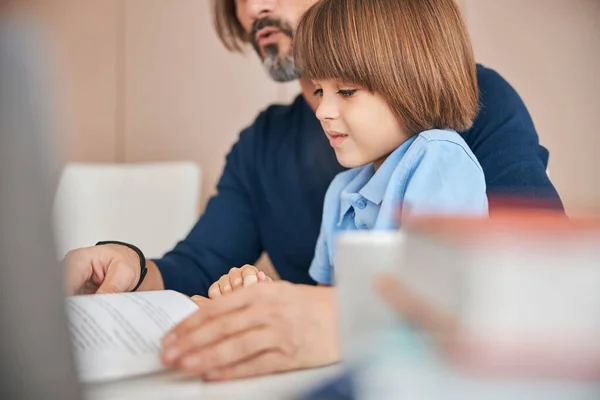 Спокойный мальчик и его родитель делают домашнее задание вместе — стоковое фото