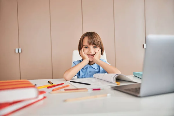 Mirthful child at the table with stationery supplies on it — Stock Photo, Image