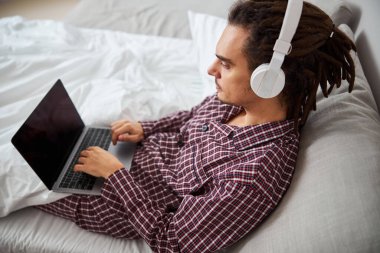 Yakışıklı genç adam yatakta uzanıyor ve modern defter kullanıyor.