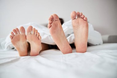 Çıplak ayakla yatakta dinlenen genç bir çift.