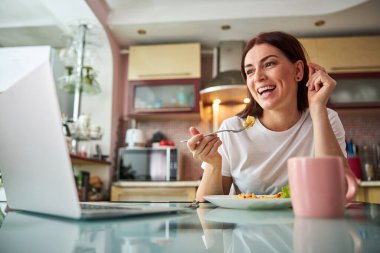Ev hanımı laptopuna bakarken yemeğinin tadını çıkarıyor.