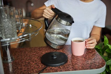 Çaydanlığı suyla birlikte çay fincanına yatıran kişi.