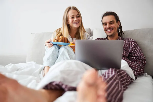 这对漂亮的夫妇使用笔记本电脑，在床上吃早餐 — 图库照片