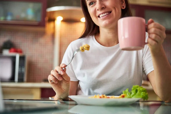 Husmor som løfter en tekopp mens hun sitter over måltidet – stockfoto