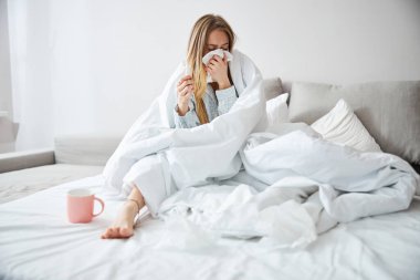 Hasta genç bir kadın evdeki kağıt peçeteye burnunu siliyor.