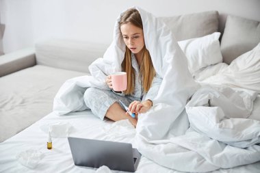 Dijital termometresi olan hasta genç kadın internette doktorla konuşuyor.