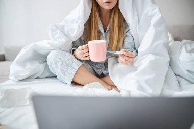 Hasta genç kadın sıcaklık değerlerini kontrol ediyor ve not defteri kullanıyor.