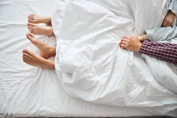 Gelukkig paar met blote voeten liggend in bed en hand in hand — Stockfoto