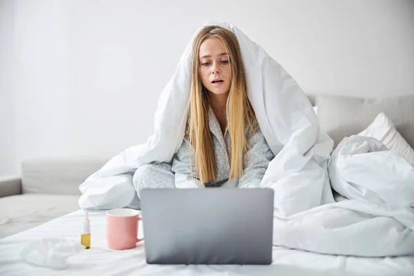 Jovem encantadora com gripe usando laptop em casa — Fotografia de Stock