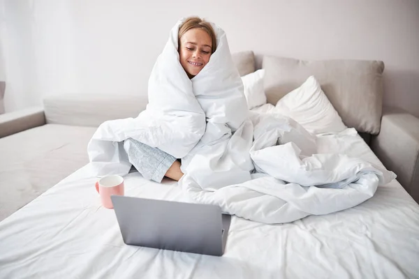 Весела молода жінка використовує ноутбук у спальні — стокове фото