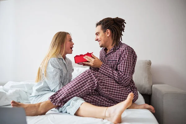 Homem alegre dando presente à namorada feliz no quarto — Fotografia de Stock