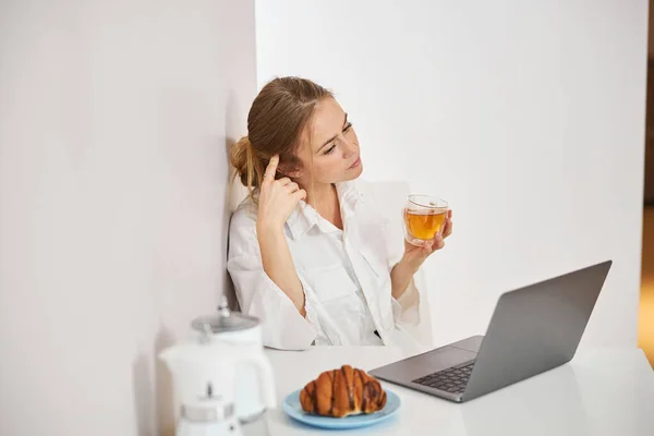 迷人的年轻女子在家里喝茶和使用笔记本电脑 — 图库照片