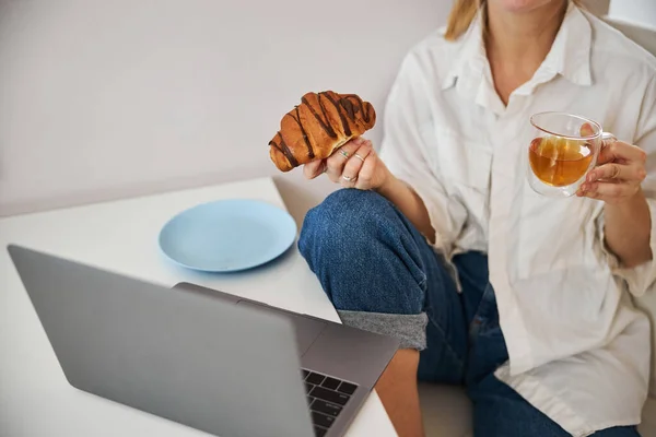 Молода жінка снідає і використовує сучасний ноутбук вдома — стокове фото