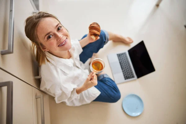 Радісна молода жінка снідає і використовує блокнот вдома — стокове фото