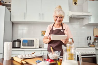 Tabletle yemek pişirmeye hazırlanan neşeli yaşlı kadın.