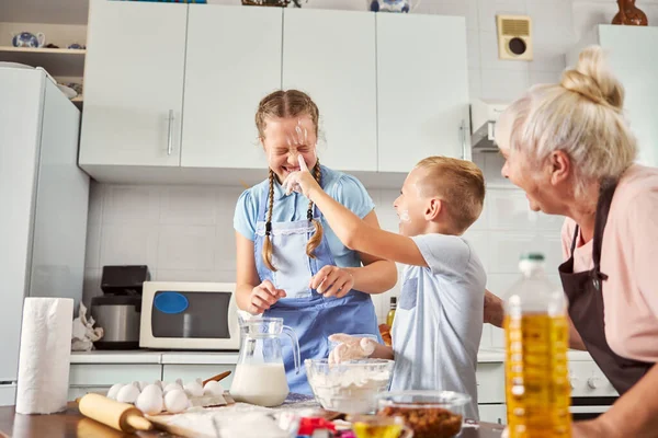 I bambini allegri che sbavano farina su ogni altra faccia in cucina — Foto Stock