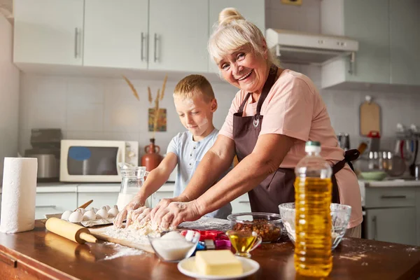 Весела старіюча леді і зосереджений хлопчик готує на кухні — стокове фото