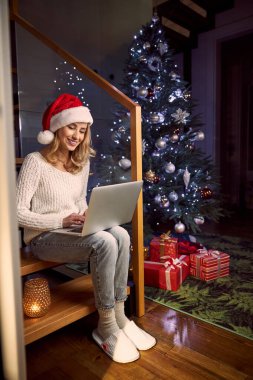 Noel Baba şapkalı çekici bir kadın. İçerideki odada online alışveriş yapıyor.