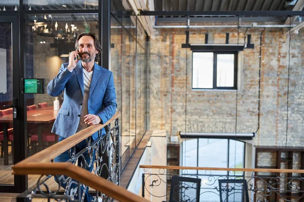 Smiley man talking on phone while standing in loft hotel — Zdjęcie stockowe