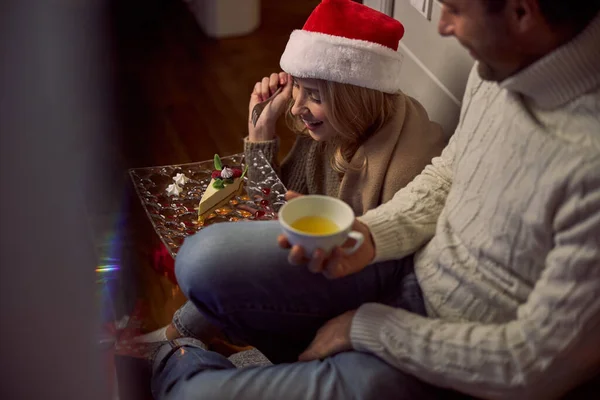 Mulher encantadora em chapéu de Santa e suéter segurando bolo saboroso na mão perto de homem bonito — Fotografia de Stock