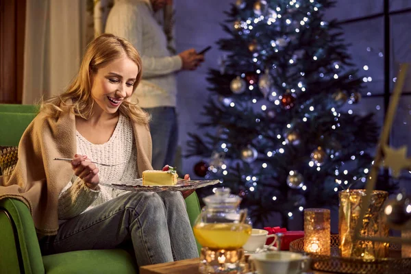 快乐的金发女人，穿着温暖的衣服，毛毯，在家里喝茶，吃着美味的甜点 — 图库照片
