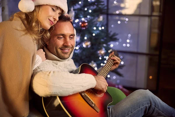 Красивий чоловік в светрі грає на гітарі для красивої жінки поруч з ним — стокове фото