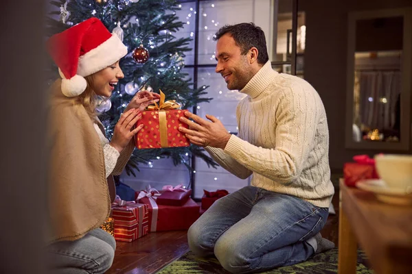 Красивий чоловік дарує подарунок для прекрасної жінки, сидячи в оздобленні різдвяної кімнати — стокове фото