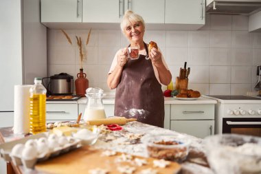 Pleased senior woman tasting homemade baked goods clipart