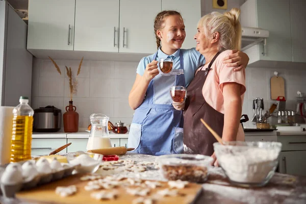 Amistosa chica dando a su abuela un gran abrazo en la cocina — Foto de Stock