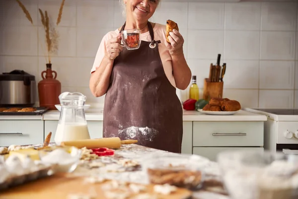 Joyeuse femme âgée essayant pâtisseries maison dans sa cuisine — Photo