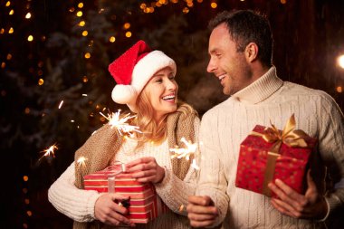 Parıldayan çam ağacının önünde kollarında maytap olan mutlu bir çift.