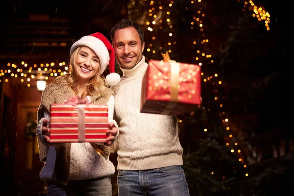 Прекрасна пара з червоними подарунковими коробками в руках насолоджується чудовим вечором на Різдво — стокове фото
