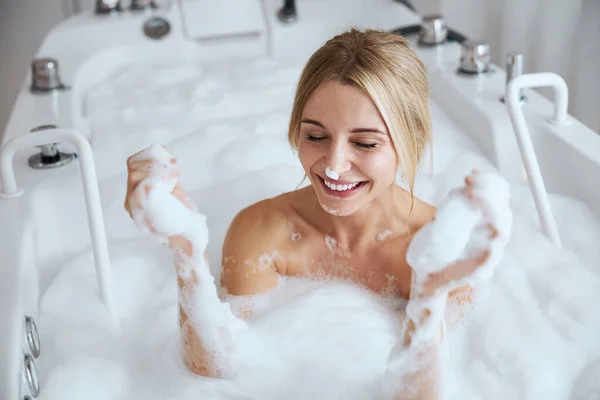 Gülümseyen genç kadın köpük banyosu yaparken eğleniyor. — Stok fotoğraf