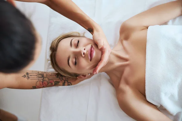 Jonge vrouw genieten van gezichtsmassage met aromatische kaarsen in spa salon — Stockfoto