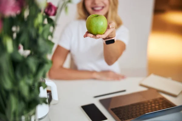 Фокусоване зображення зеленого яблука в жіночій руці над білим столом — стокове фото
