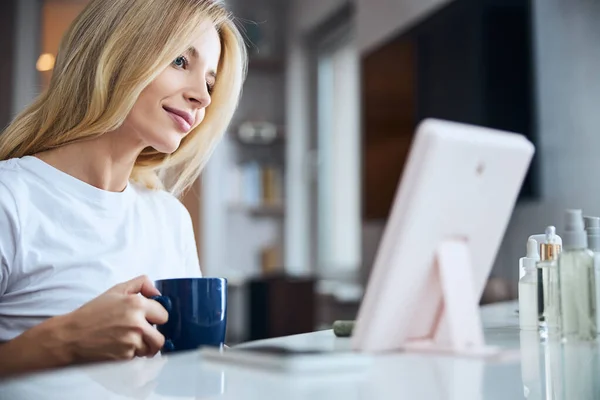Щаслива весела блондинка жінка відпочиває в домашньому офісі за чашкою чаю або кави — стокове фото