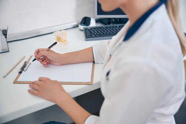Femme en uniforme médical écrivant au bureau — Photo