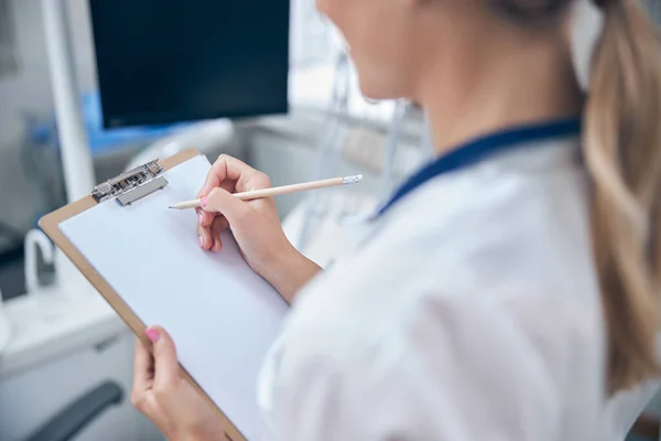 Femme dentiste écrit sur presse-papiers dans le bureau — Photo