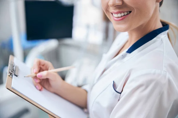 Sourire femme dentiste écriture sur presse-papiers dans la clinique — Photo