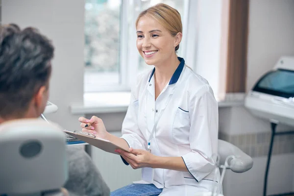 Dentiste féminine joyeuse prenant des notes sur la patiente — Photo