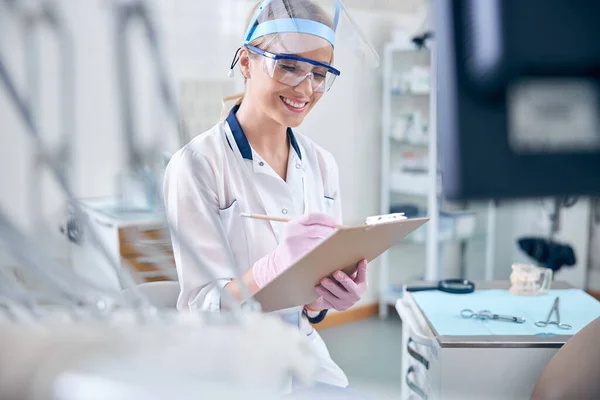 Odontóloga alegre en uniforme haciendo notas — Foto de Stock