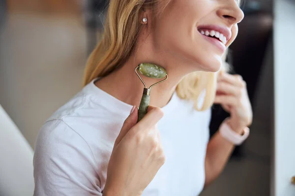 아파트 에서 비취 돌로 로울러 마사 저 를 닦고 있는 행복 한 미소짓는 젊은 아가씨 — 스톡 사진