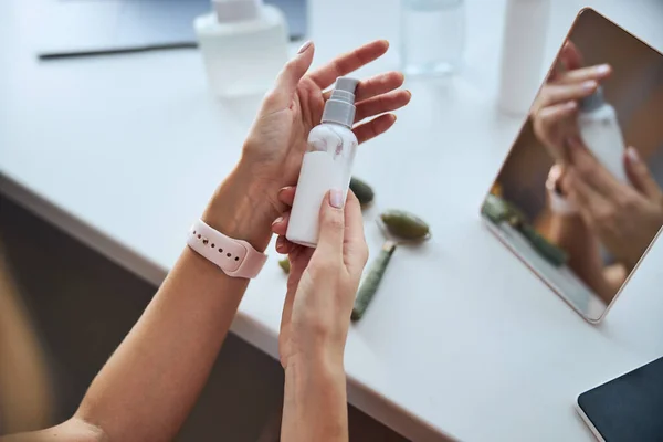 Beautiful female holding moisturize emulsion in front of the mirror — Stock Photo, Image